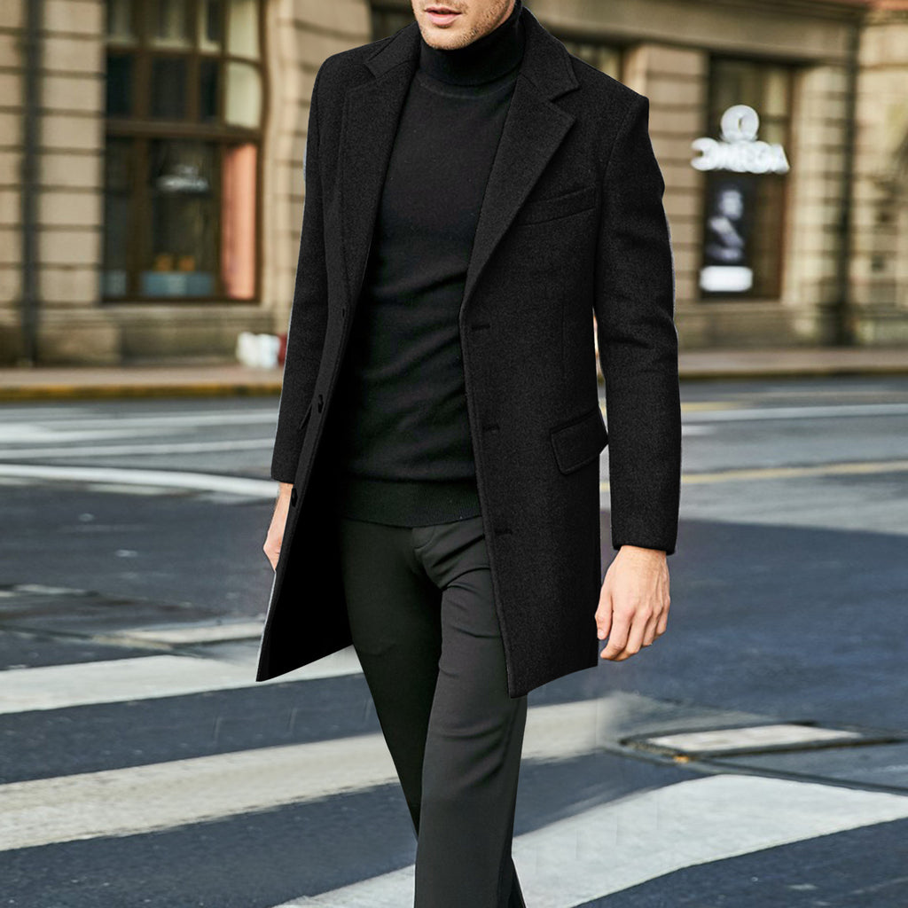 Man wearing a black coat and black turtleneck walking on a city street.