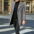 Man wearing a gray coat over a black turtleneck and pants on a city street.