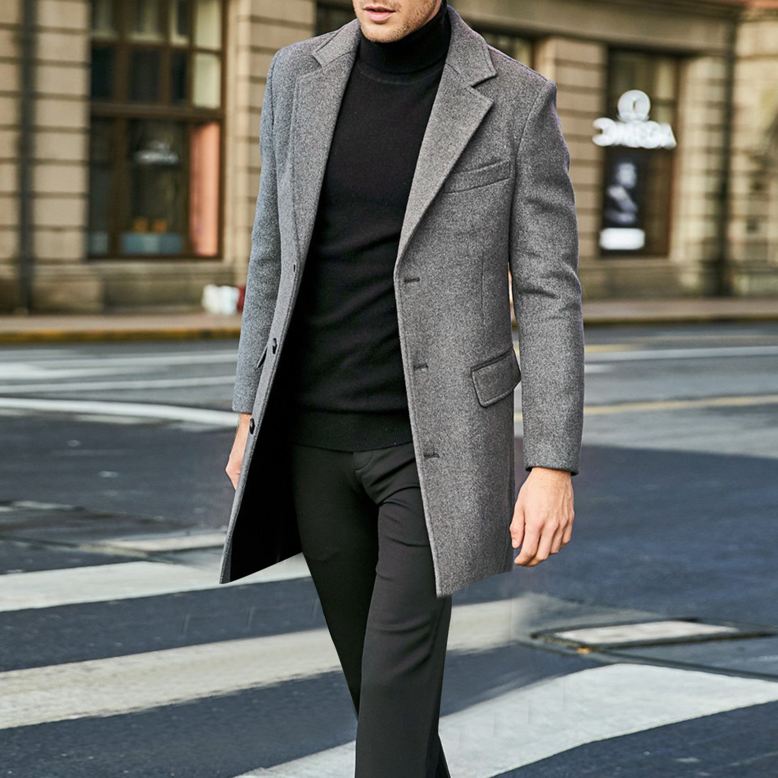 Man wearing a gray coat over a black turtleneck and pants on a city street.